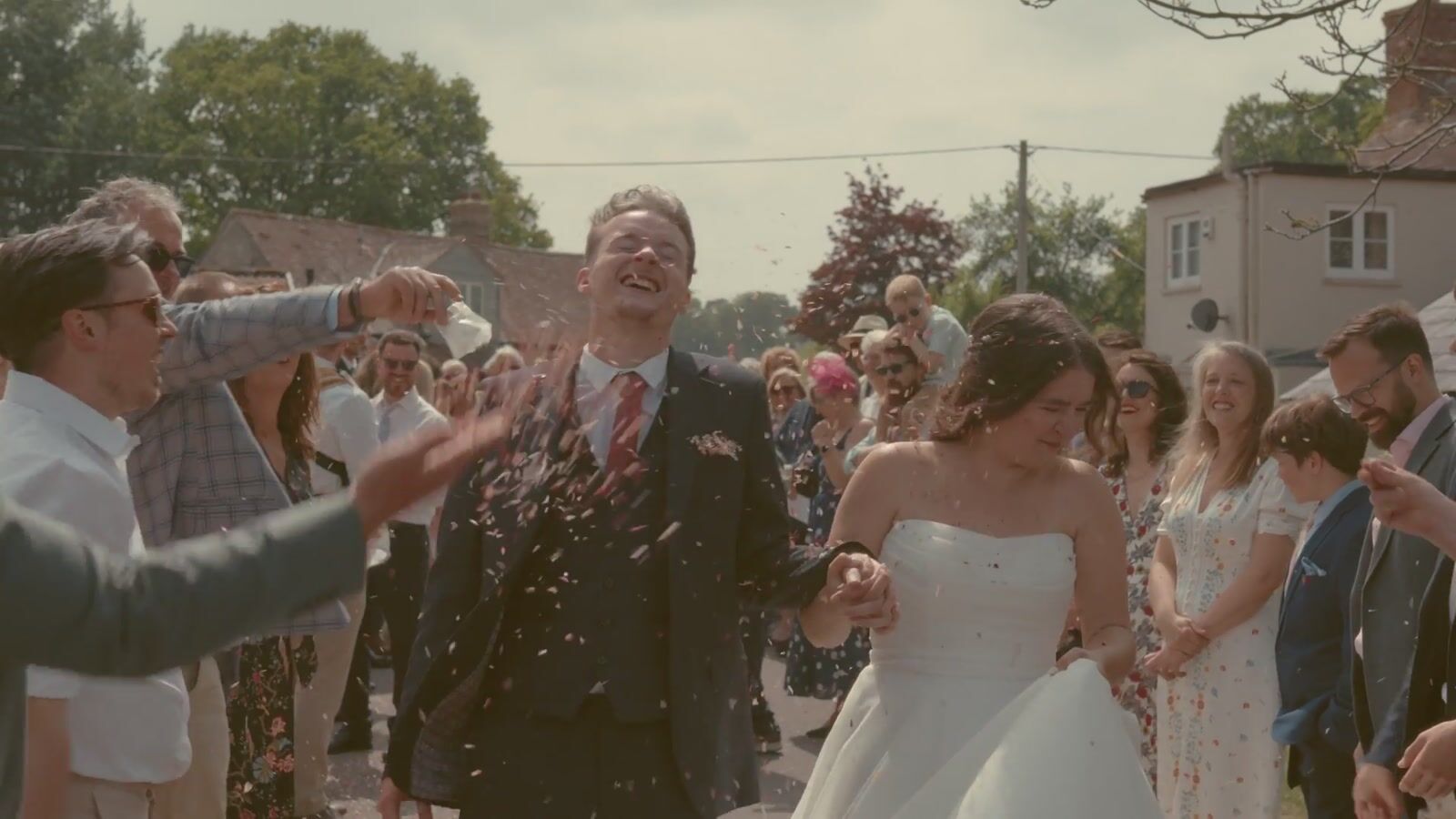A newly married couple surrounded by smiling guests and confetti.